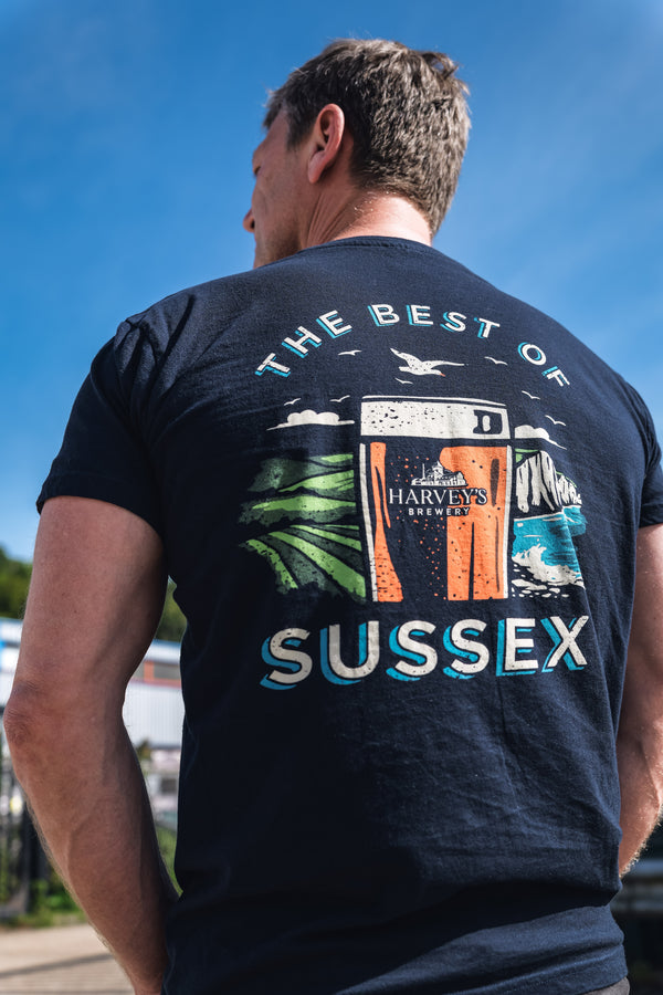 Man wearing a blue harvey's t-shirt with 'The Best of Sussex' graphic design outdoors.
